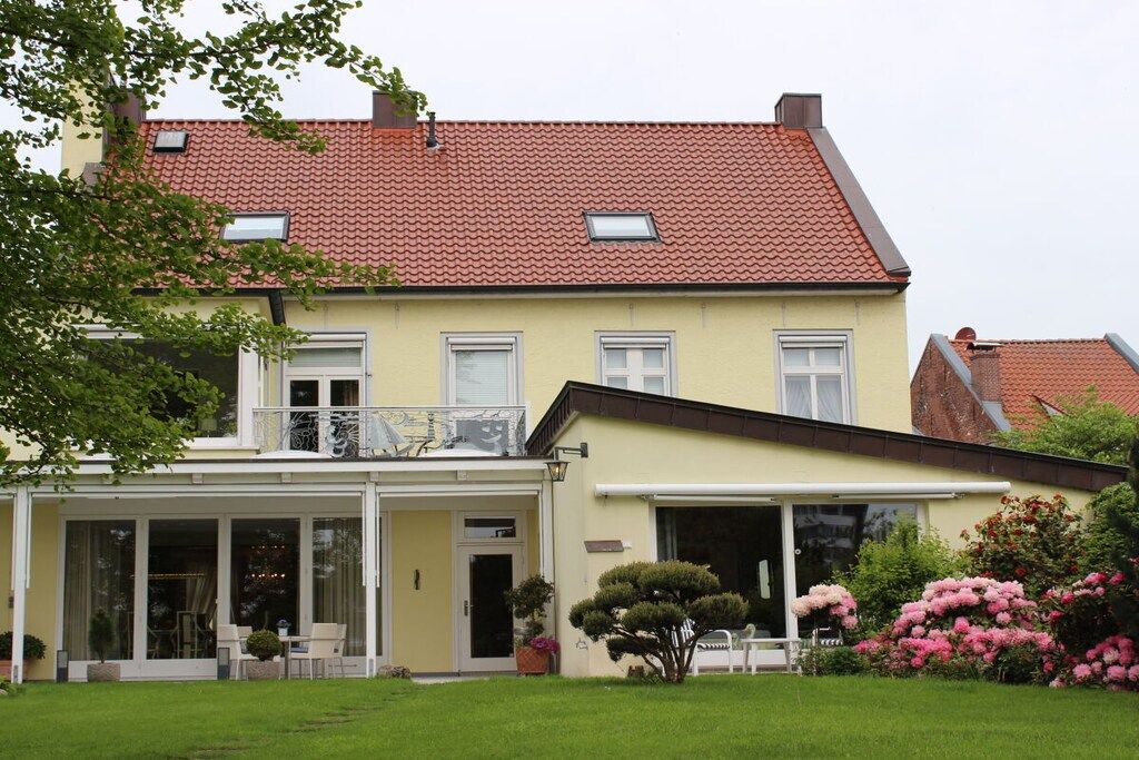 Een gebouw met twee verdiepingen, een rode pannendak, een balkon en een overdekte veranda met stoelen.
