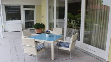 A patio with a table and chairs, a potted plant, and a sliding glass door.