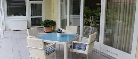 A patio with a table and chairs, a potted plant, and a sliding glass door.