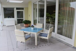 Une terrasse avec une table et des chaises, un pot de fleurs et une porte-fenêtre coulissante.