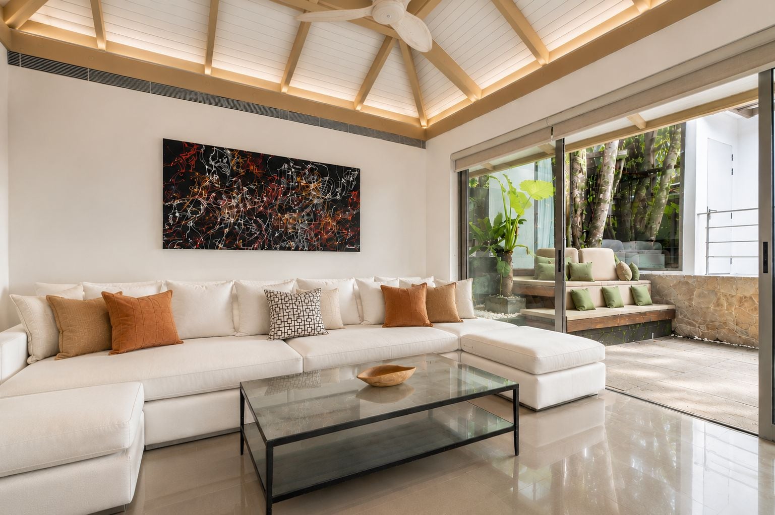 A modern living room with a sectional sofa, a glass coffee table, and a large abstract painting on the wall.