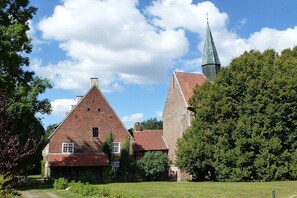 A traditional brick building with a steeply pitched roof and a visible church steeple in the background. - Holiday home with 1 bedroom (Berge OT Börstel)