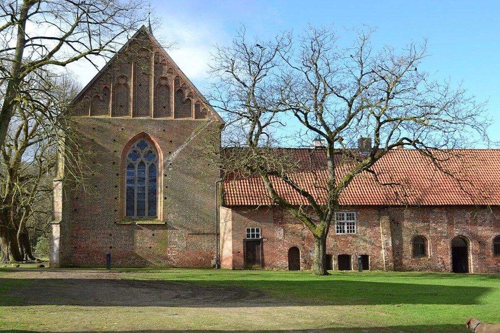 Un bâtiment historique doté d’une tour imposante et de fenêtres en arc de cercle, entouré d’une pelouse et d’arbres.