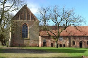 A historic building with a prominent tower and arched windows, surrounded by a grassy area and trees. - Holiday home with 1 bedroom (Berge OT Börstel)