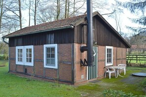 A small brick building with a tiled roof, a chimney, and a small outdoor seating area with a table and chairs. - Holiday home with 1 bedroom (Berge OT Börstel)