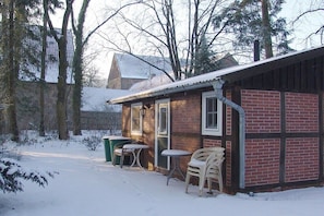 A small brick building with a metal roof, a door, and windows. There are two outdoor tables and chairs. - Holiday home with 1 bedroom (Berge OT Börstel)