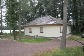 Ein kleines, eingeschossiges Gebäude mit einem Ziegeldach, umgeben von Bäumen und einem Kiesweg.