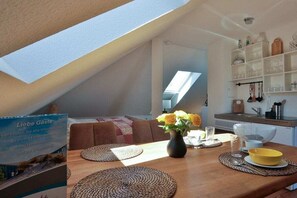 Ein Essbereich mit Tisch für zwei Personen, einer Blumenvase und einer Küche im Hintergrund.