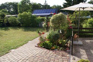 A garden area with a paved walkway, a solar panel array, and a wooden pergola with a table and chairs. - Holiday home in Arendsee with swimming pool (Arendsee)