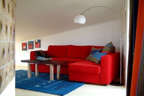 Ein rotes Sofa, ein Couchtisch aus Holz, ein blauer Teppich und eine weiße Stehlampe.