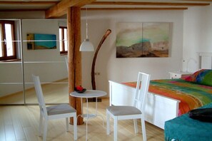 Ein Schlafzimmer mit einem Bett, einem Schreibtisch, zwei Stühlen, einem Tisch und einem Gemälde an der Wand.