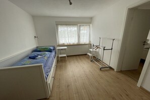 A small, single-room apartment with a bed, a radiator, a window with curtains, and a door. - Holiday apartment with 2 bedrooms (Waldshut-Tiengen)