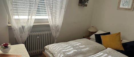 A bedroom with a bed, bedside table, lamp, and a window with sheer curtains.