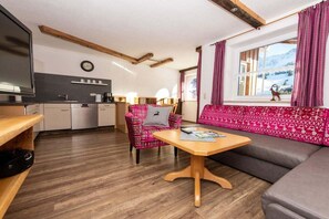 A cozy interior with a wooden floor, a sofa, a chair, a table, and a kitchen area with a window. - Iseler - Landhaus Thomma (Oberjoch)