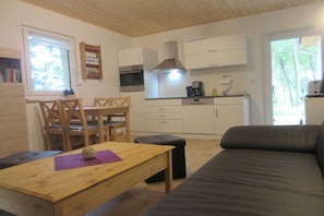 A compact living space with a kitchenette, a dining area with wooden chairs, a sofa, and a small table with a purple placemat. - B 3 directly at Lake Netzen (Kloster Lehnin OT Trechwitz Siedling)