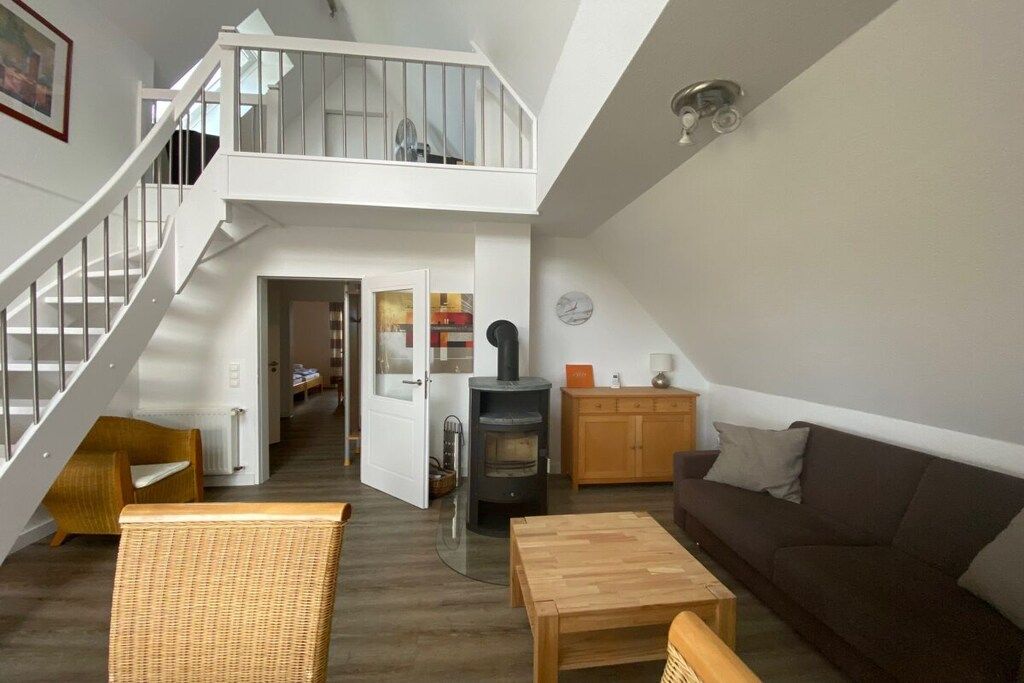 Ein großzügiger Wohnbereich mit einer Treppe zu einem Schlafzimmerloft, einem Kaminofen und einer gemütlichen Sitzecke.