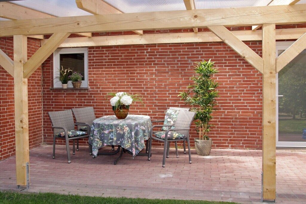 Een overdekt terras met een bakstenen muur, een tafel met stoelen en potplanten.