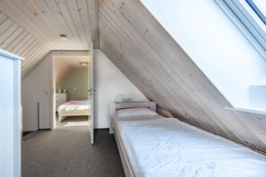 Una camera da letto con soffitto a falde, un letto, un comodino e una cassettiera.