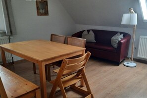 Una habitación con una mesa de comedor de madera, dos sillas, un sofá rojo y una lámpara de pie.