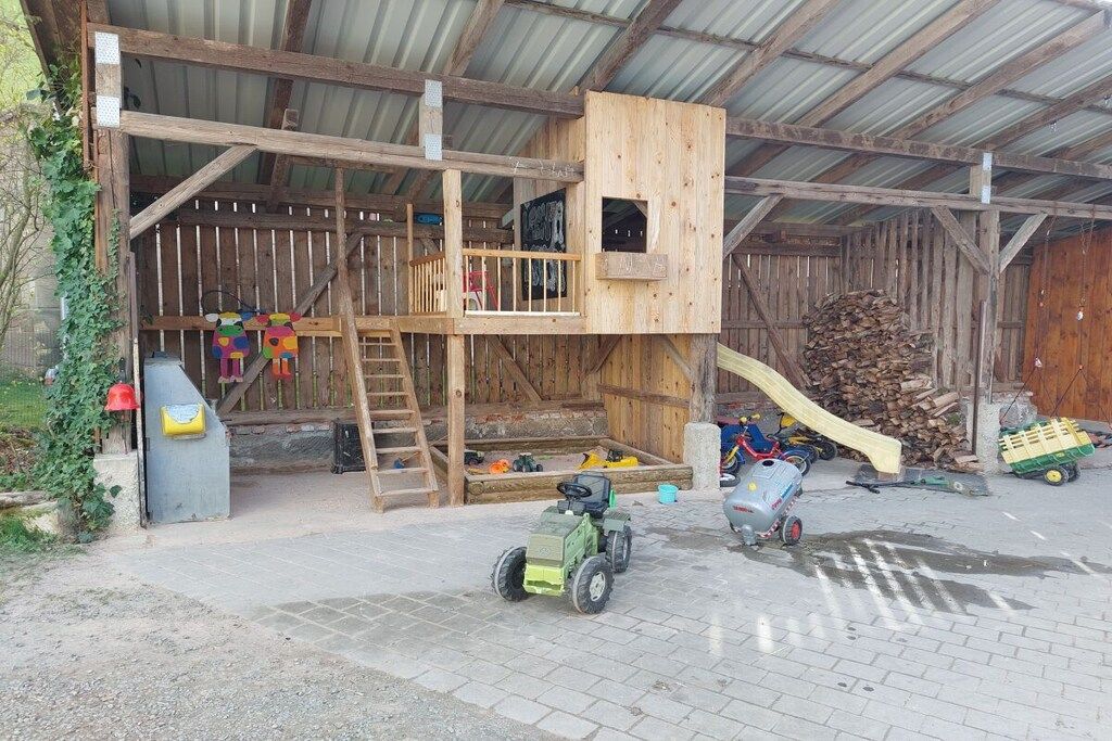 Ein rustikaler Schuppen mit einem hölzernen Spielhäuschen, einer Rutsche und einem Traktor.