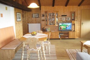 A wooden interior with a dining table, chairs, a television, and a cabinet with glass doors. - Holiday apartment with 1 bedroom (Wegscheid)