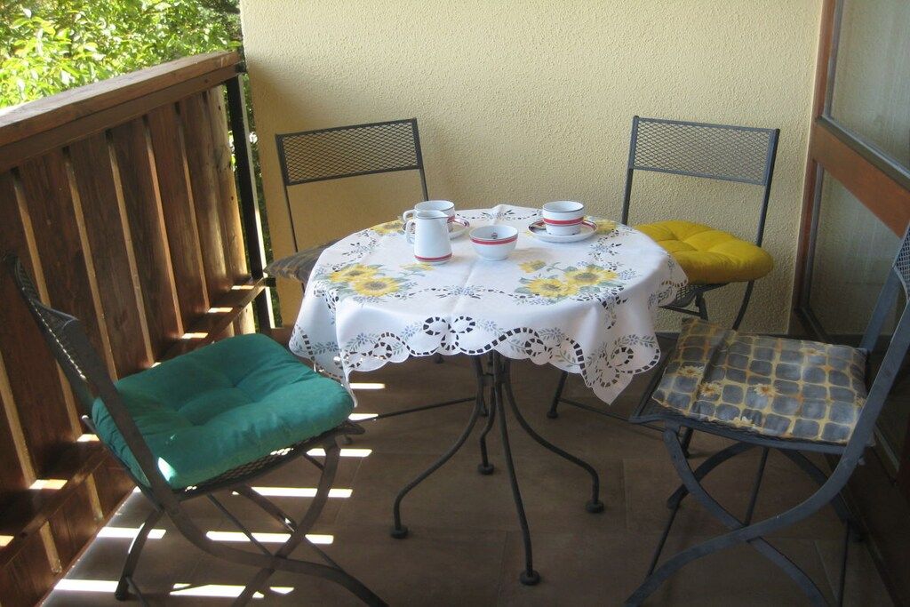 A patio with a round table covered by a floral tablecloth, two chairs with cushions, and a metal chair with a cushion.