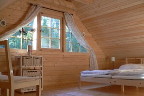 A wooden cabin room with a bed, a chair, a small table, and a window with curtains.
