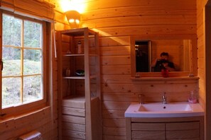 A wooden cabin interior with a window, a sink, and a mirror.