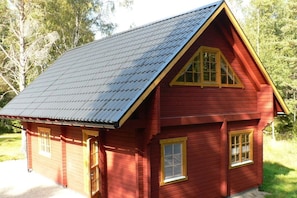 A red wooden cabin with a gabled roof and a single front door.