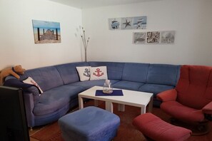 A living room with a blue sofa, a red armchair, a white coffee table, and a television. - Holiday home with 1 bedroom (Visselhövede)