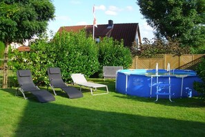 A backyard with a swimming pool, two lounge chairs, and a wooden fence. - Holiday home with 1 bedroom (Visselhövede)