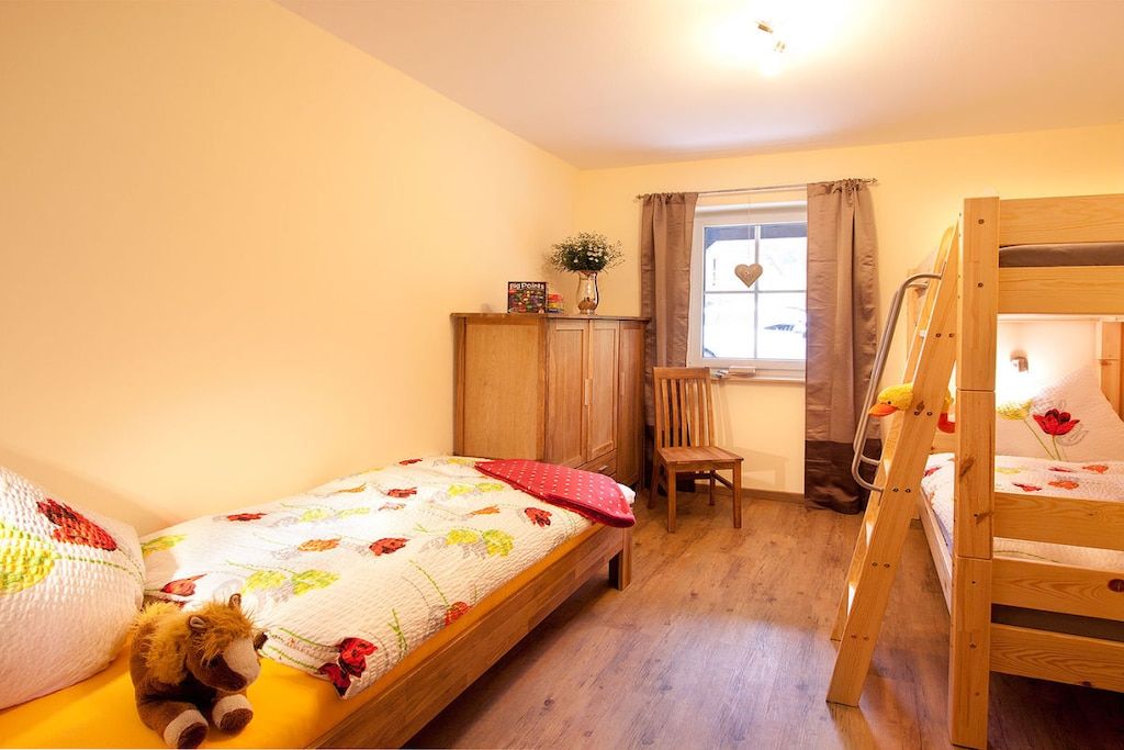 Un dormitorio con una litera, una cama individual, un armario de madera, un escritorio con silla y una ventana con cortinas.