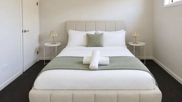 A neatly made bed with white bedding and a green throw, two bedside lamps, and a door to the left.