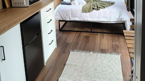 A modern bedroom with a bed, bedside table, and a built-in desk with a microwave.