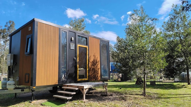 A modern, compact cabin with a wooden exterior, a glass door, and a small outdoor seating area.
