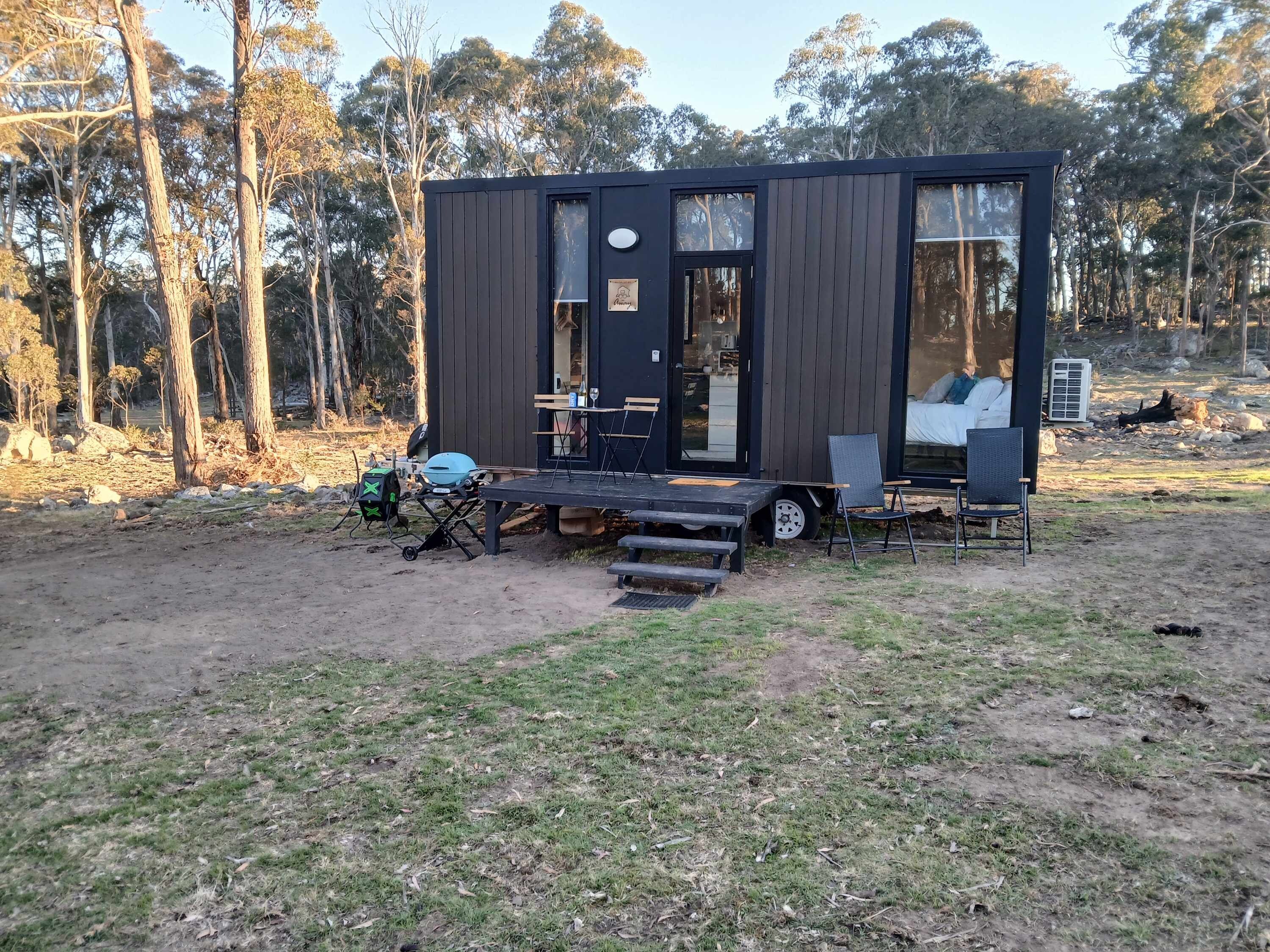 A small cabin with a deck, a grill, and outdoor seating.