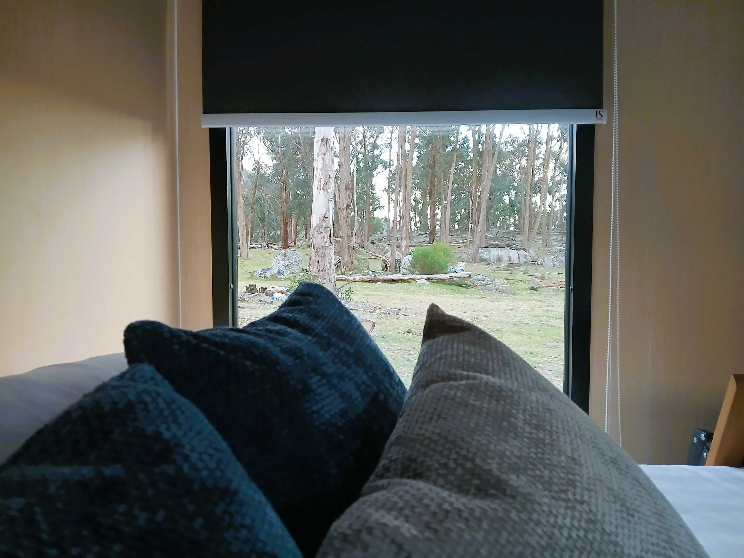 En säng med kuddar och ett fönster med utsikt över en skog.