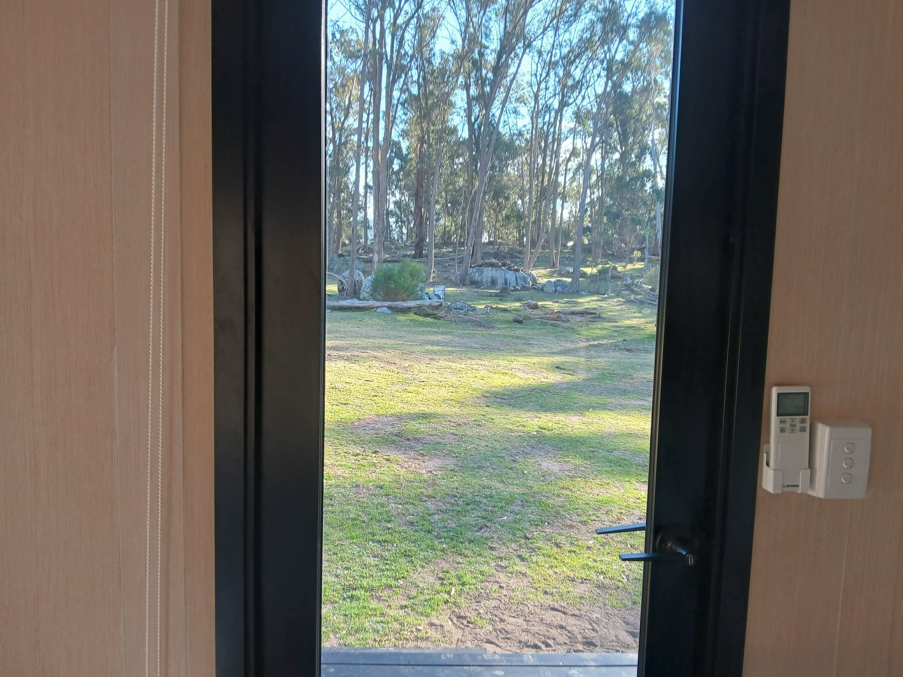 A view through a door with a digital lock, leading to an outdoor area with grass and trees.