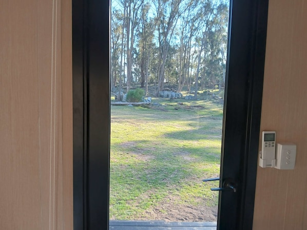 A view through a door with a digital lock, leading to an outdoor area with grass and trees.