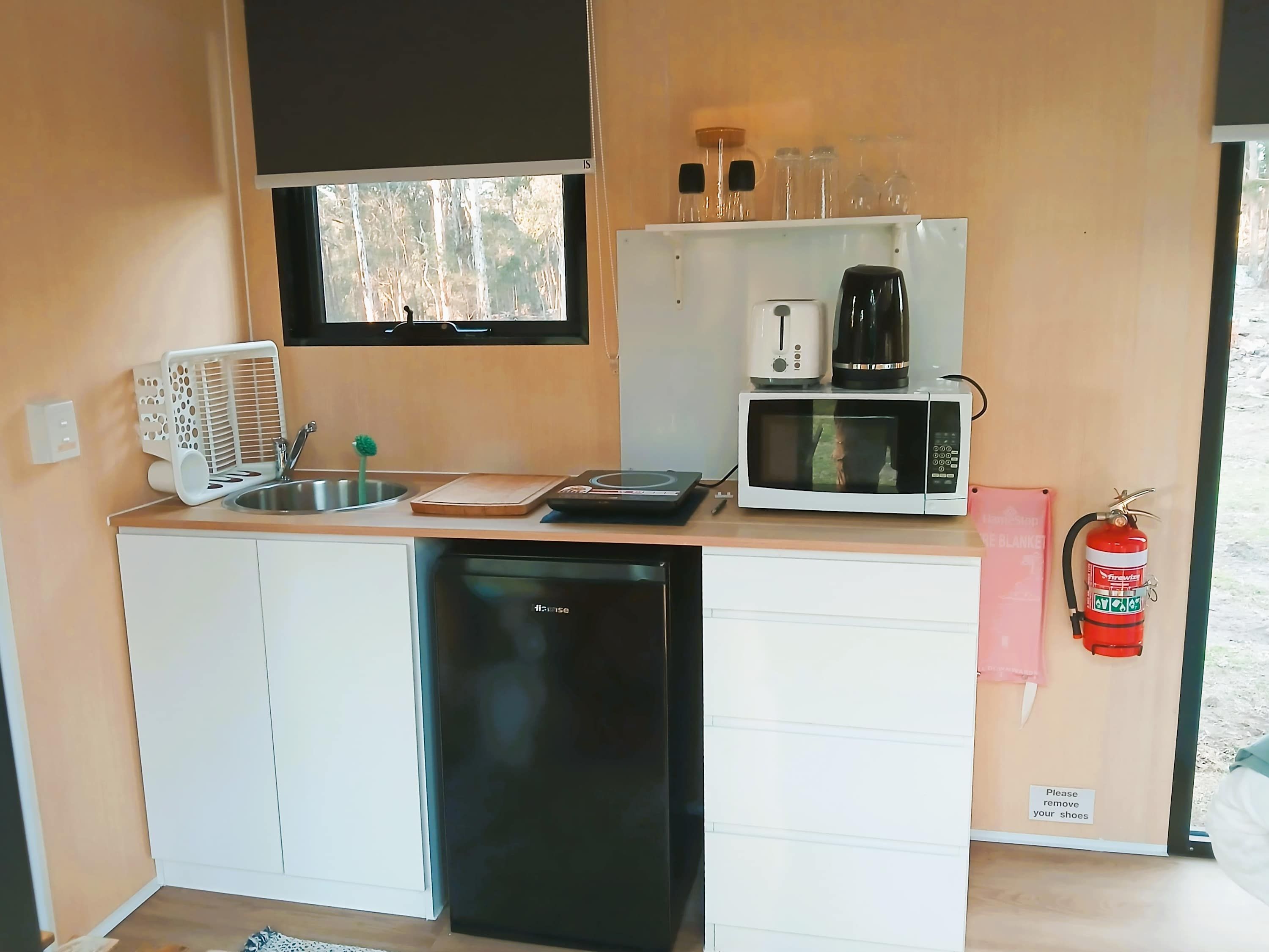 Cocina compacta con lavavajillas, microondas, cafetera y ventana con vista a árboles.