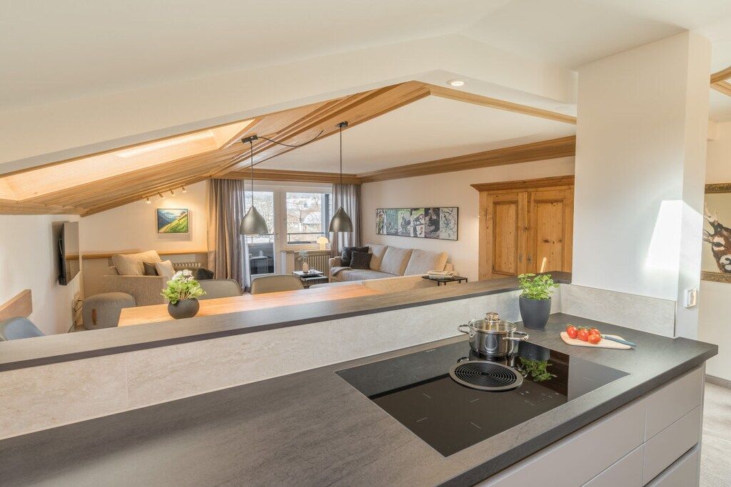 A modern kitchen with a central island, wooden ceiling beams, and a dining area with a sofa and table.