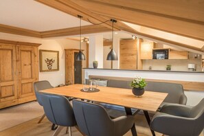 A modern kitchen with wooden cabinets, a dining table with chairs, pendant lighting, and a microwave. - Holiday apartment in Oberstdorf with balcony (Oberstdorf)
