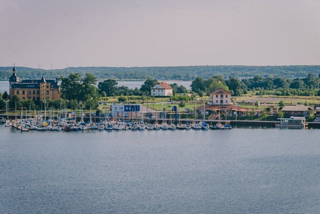 Un port de plaisance avec des bateaux, un grand bâtiment et des maisons d’habitation le long du rivage.