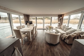 A modern interior with a dining area, sofa, and large windows overlooking a body of water.