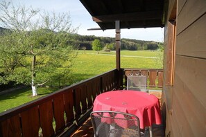 A wooden deck with a table and chairs, overlooking a green field and trees. - Holiday apartment with 1 bedroom (Bernau am Chiemsee)