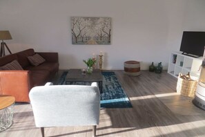 Ein Wohnzimmer mit einer Couch, einem Couchtisch, einem Fernseher und einem Gemälde an der Wand.