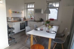 Eine moderne Küche mit Esstisch, Stühlen und einer kleinen Kochinsel mit Kaffeemaschine.