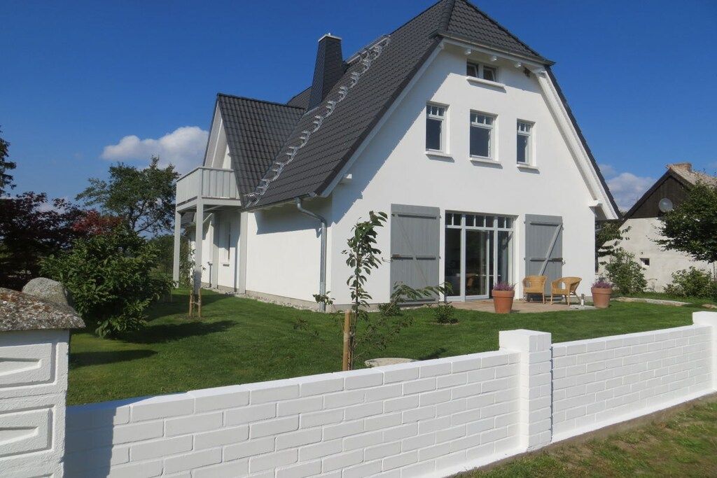 Una casa de dos pisos con techo inclinado, un porche con sillas y una valla blanca.
