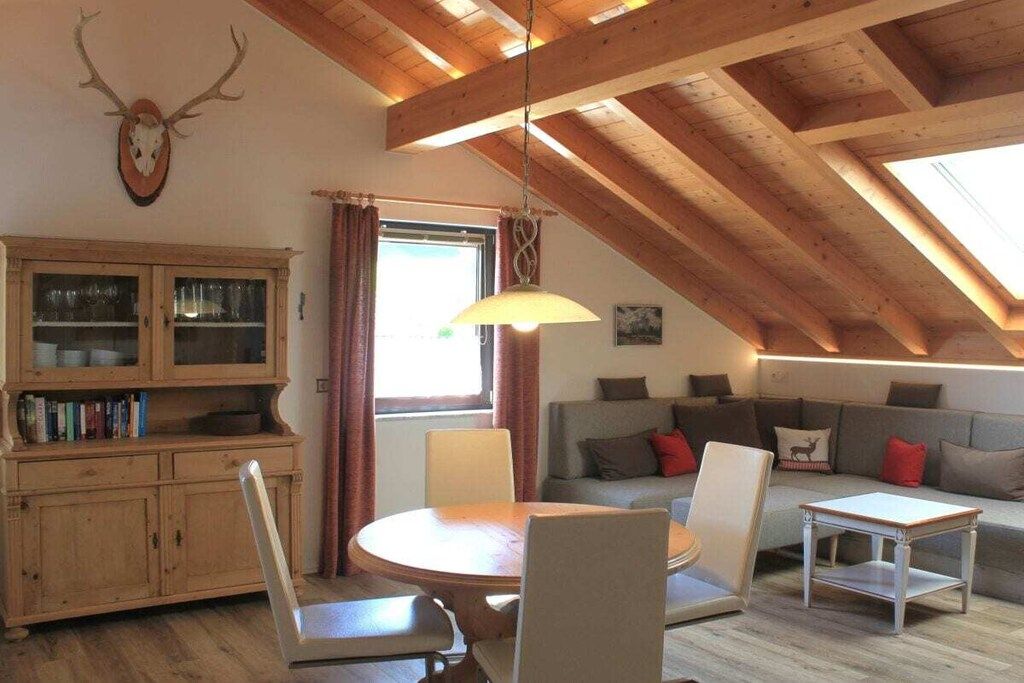 Una habitación acogedora con techo de madera, una mesa redonda con sillas, un sofá y un aparador con puertas de cristal.
