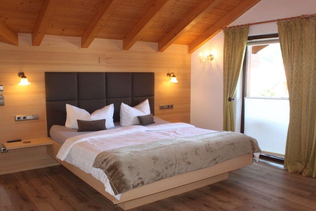 Un dormitorio con cama, techo de madera, luces fijadas a la pared y una ventana con cortinas.